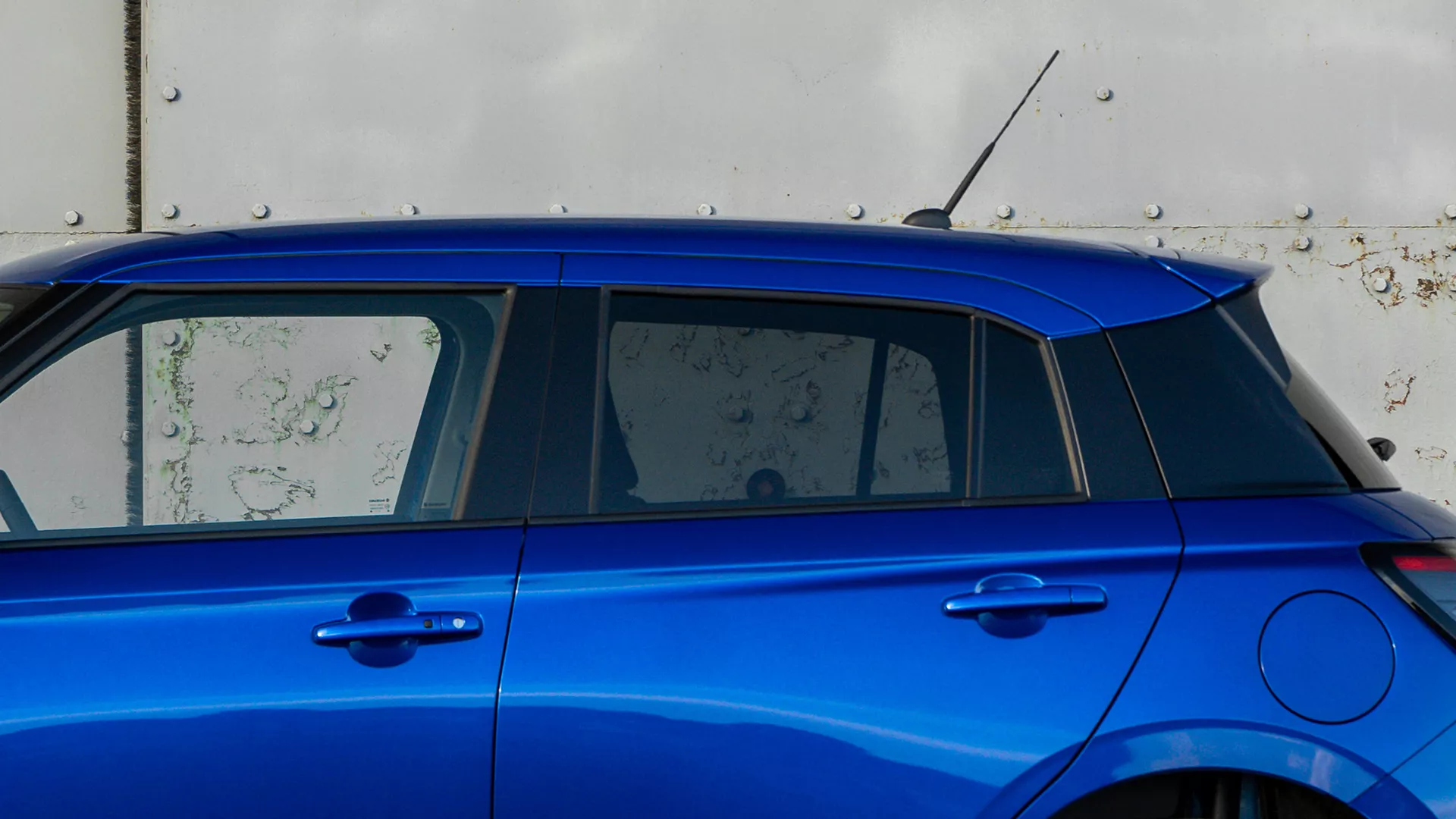 Side view of the Suzuki Swift highlighting its distinctive floating roof design with blacked-out pillars and vibrant blue body