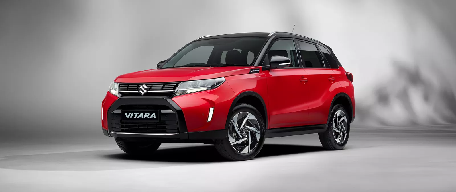 Front and side view of the Suzuki Vitara in bright red with a cosmic black roof, showcasing its bold SUV styling and distinctive alloy wheels.