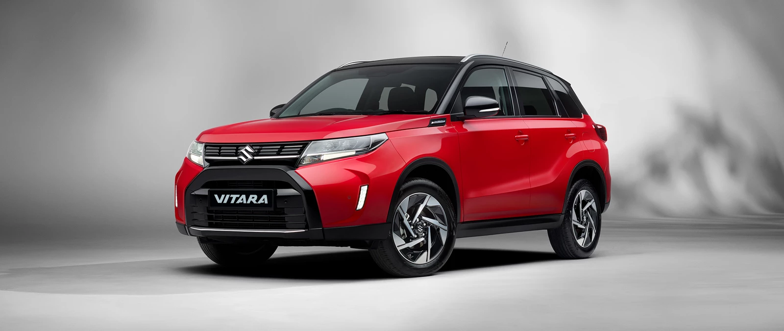 Front and side view of the Suzuki Vitara in bright red with a cosmic black roof, showcasing its bold SUV styling and distinctive alloy wheels.
