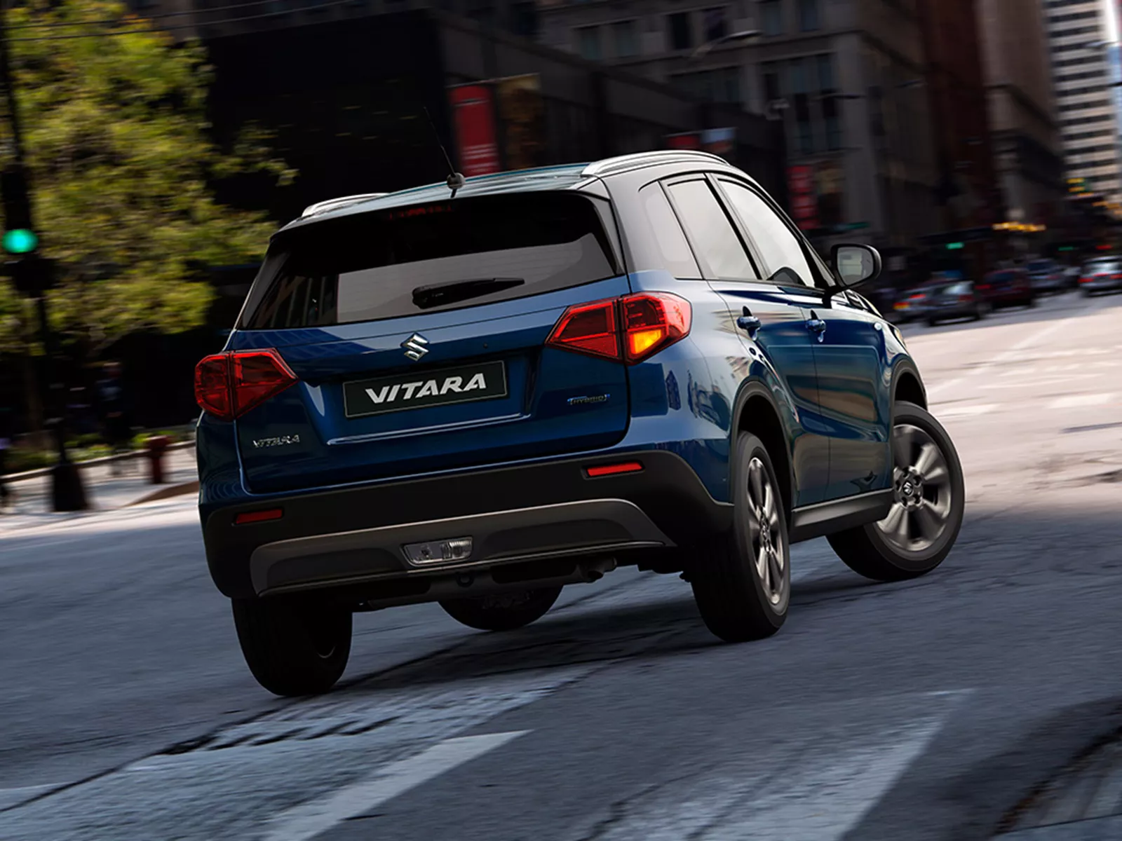 Rear view of the Suzuki Vitara in sphere blue driving through a city street, showcasing its urban styling and compact SUV design.