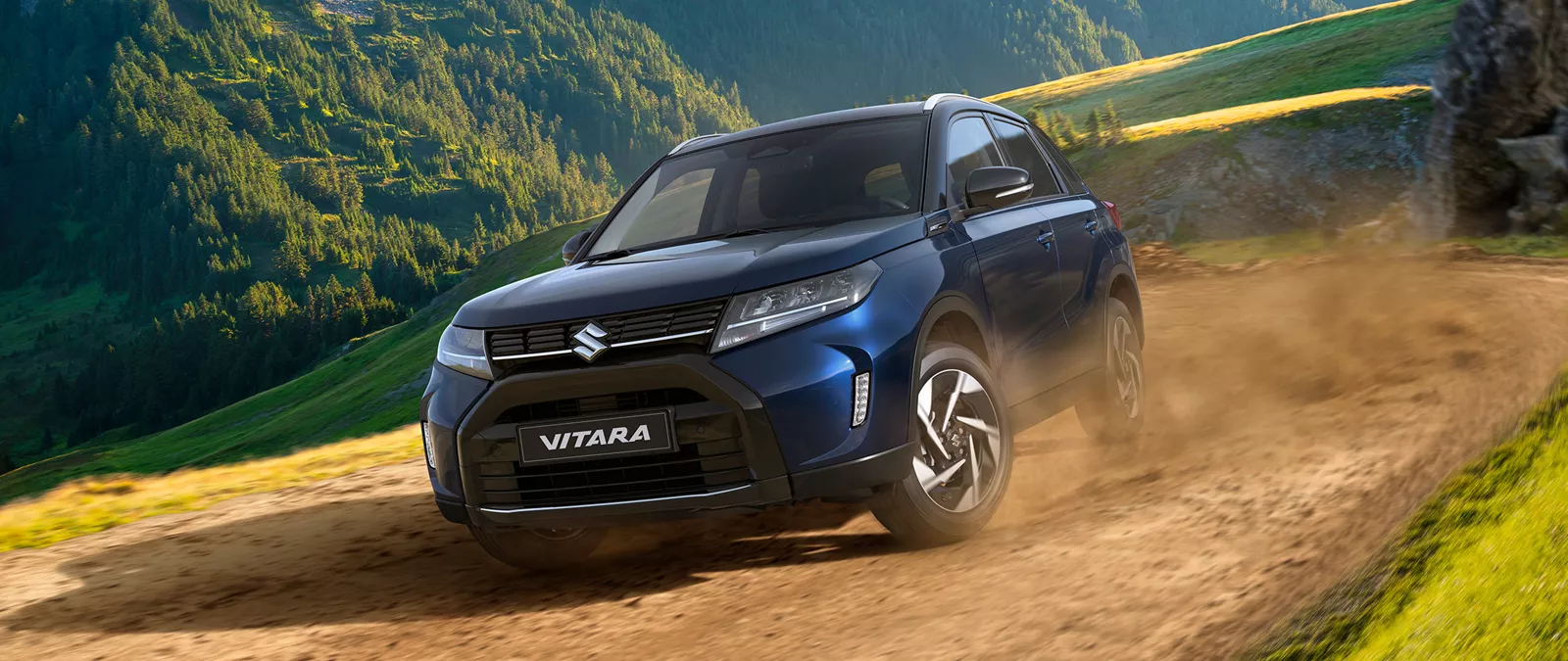 Front and side view of the Suzuki Vitara in blue driving off-road on a dirt track, highlighting its rugged capability and SUV performance.